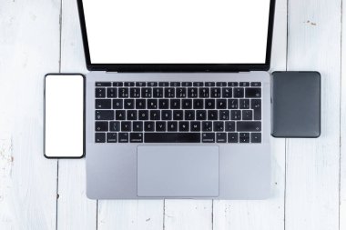 Laptop ve beyaz ahşap masadaki boş ekranlı telefon. Çalışma alanı. Boşluğu kopyala.