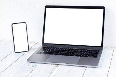 Laptop ve beyaz ahşap masadaki boş ekranlı telefon. Çalışma alanı. Boşluğu kopyala.