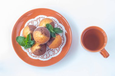 Bir fincan çay ile beyaz bir tabloda turuncu tabakta cupcakes