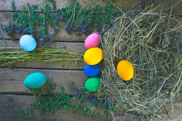 Multi-colored Easter eggs on a wooden background in the nest. — Stock Photo, Image