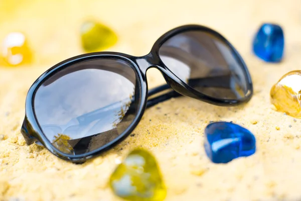 在沙地海滩上的黑色太阳镜. — 图库照片