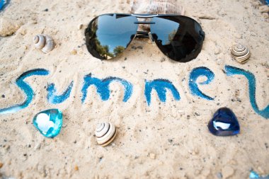 Güneşli kumlu bir plaj üzerinde siyah güneş gözlüğü.