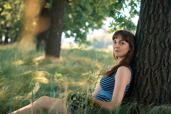 Glad flicka sitter under ett träd på en sommar. — Stockfoto