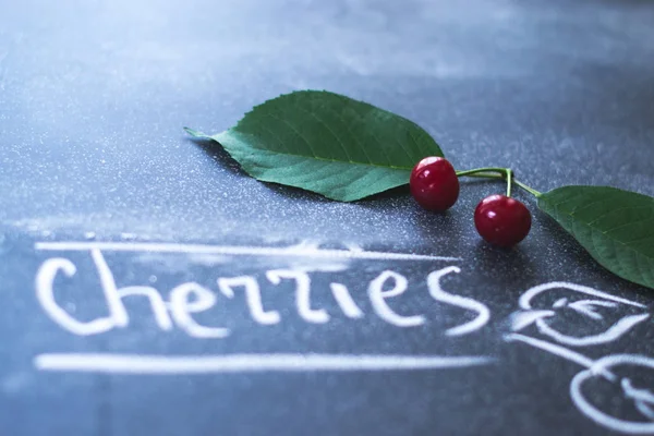 Cherries on a black matte background with chalk text.