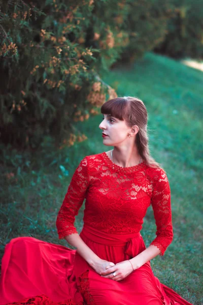 Belle jeune fille dans une robe rouge herbe siège . — Photo