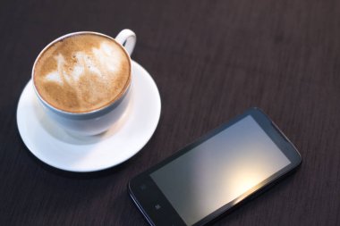 Bir fincan kahve, bir akıllı telefon ile arka plan bulanık bir kafede.