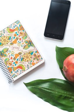 Not etmek üstünde beyaz bir arka plan ile telefon ve bir yaprak bir tropikal bitki.