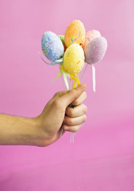 Paskalya yumurtaları pembe bir arka plan üzerinde bir sopa tutan adam