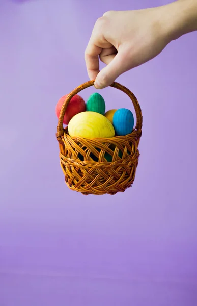 Корзина с пасхальными яйцами в руке на фиолетовом фоне — стоковое фото