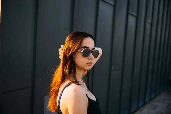 Сексуальная девушка возле темной стены в футболке, солнцезащитных очках и коротких шортах — стоковое фото