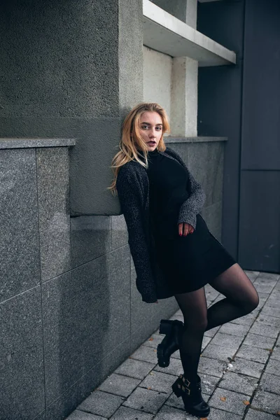 Menina em um vestido preto no inverno em um fundo de um edifício escuro — Fotografia de Stock