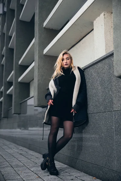 Menina em um vestido preto no inverno em um fundo de um edifício escuro — Fotografia de Stock