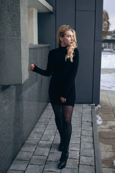 Chica en un vestido negro en el invierno sobre un fondo de un edificio oscuro — Foto de Stock