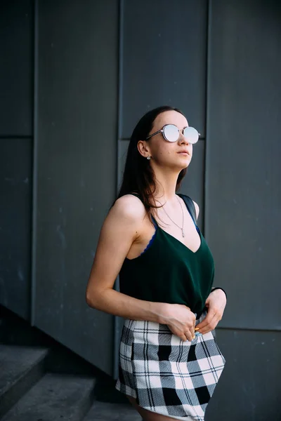 Chica sexy cerca de una pared oscura en una camiseta, gafas de sol y pantalones cortos — Foto de Stock