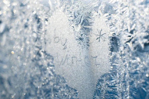 L'inscription : au revoir, hiver. Sur une fenêtre d'hiver gelée aux motifs givrés — Photo