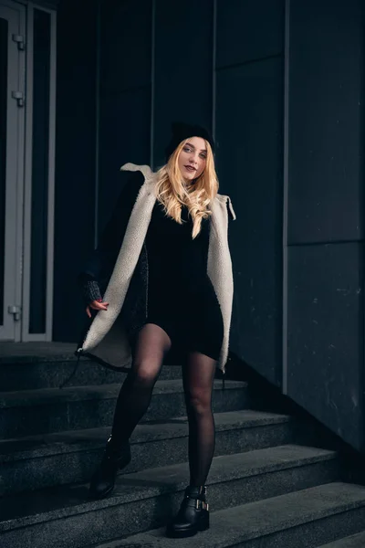 Chica en un vestido negro en el invierno sobre un fondo de un edificio oscuro —  Fotos de Stock
