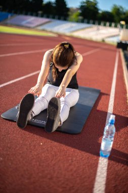Güneşli bir günde açık havada esneme egzersizleri yapan bir kız sporcu.