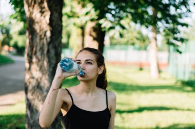 Sporcu kız parkta idmandan sonra su içer.