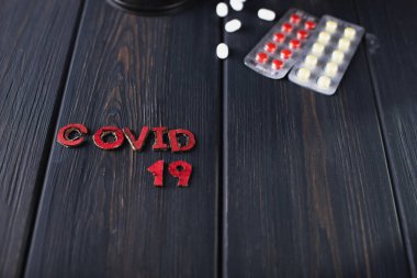 Koyu ahşap arka planda COVID-19 yazılı haplar.
