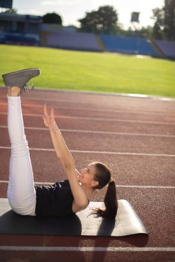 Güneşli bir günde açık havada esneme egzersizleri yapan bir kız sporcu.