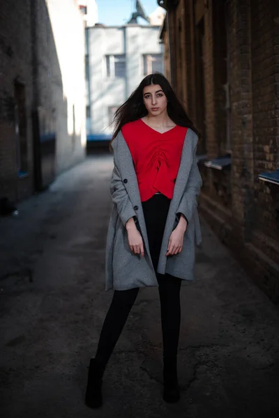 Chica en una blusa roja y un cárdigan gris en el fondo de la vieja pared de ladrillo —  Fotos de Stock