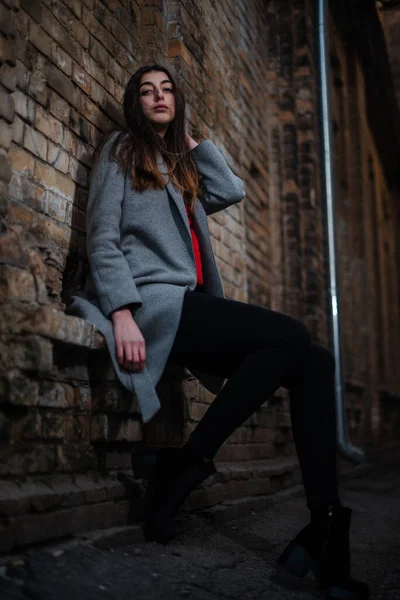 Girl in a red blouse and a gray cardigan on the background of the old brick wall — Stock Photo, Image