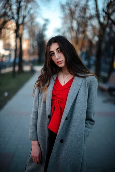 Dziewczyna w czerwonej bluzce i szarym kardiganie na rozmytym tle miasta wczesną wiosną — Zdjęcie stockowe