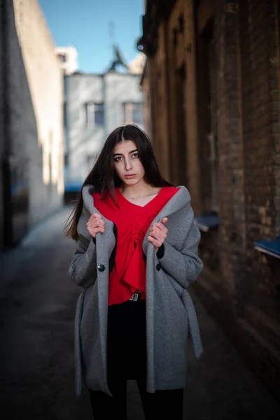 Menina em uma blusa vermelha e um casaco cinza no fundo da parede de tijolo velho — Fotografia de Stock