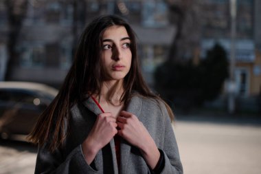 Kırmızı bluzlu ve gri hırkalı bir kız. Bulanık bir şehrin arka planında.