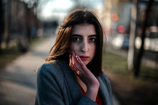 Girl in a red blouse and a gray cardigan on a blurry city background in early spring — Stock Photo, Image