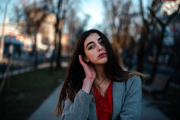 Girl in a red blouse and a gray cardigan on a blurry city background in early spring — Stock Photo, Image