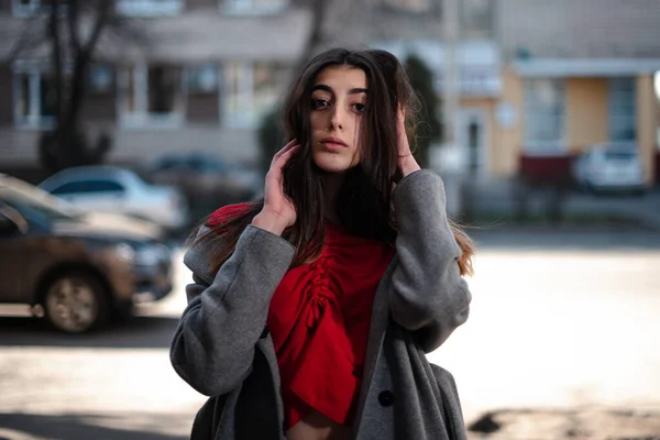 Mädchen in roter Bluse und grauer Strickjacke vor verschwommenem Stadthintergrund im frühen Frühling — Stockfoto