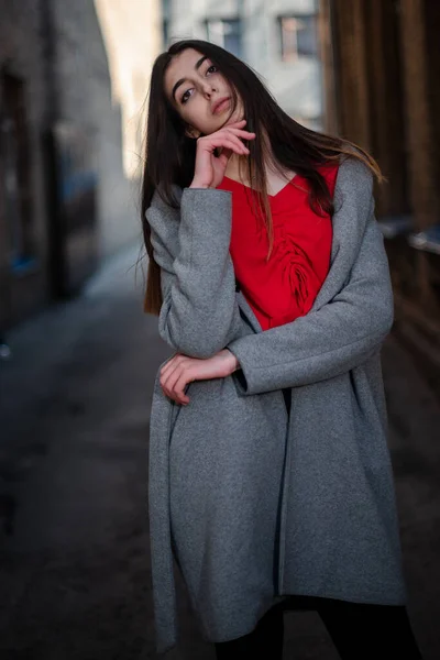 Chica en una blusa roja y un cárdigan gris en el fondo de la vieja pared de ladrillo —  Fotos de Stock