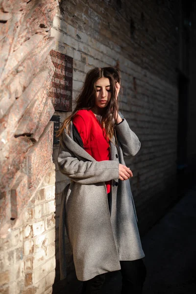 Girl in a red blouse and a gray cardigan on the background of the old brick wall — Stock Photo, Image