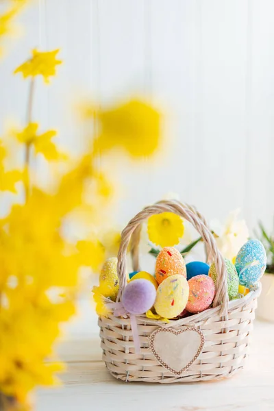 Multi-colored Easter eggs in a basket on a white wooden background