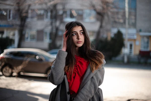 Girl in a red blouse and a gray cardigan on a blurry city background in early spring — Stock Photo, Image