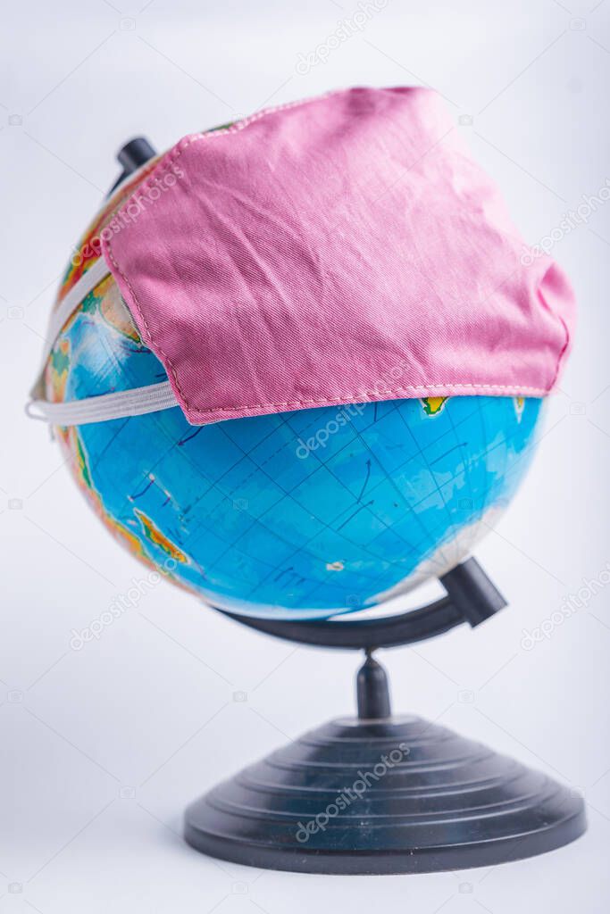 Globe in a medical mask on a light blurry background. Coronavirus pandemic protection concept