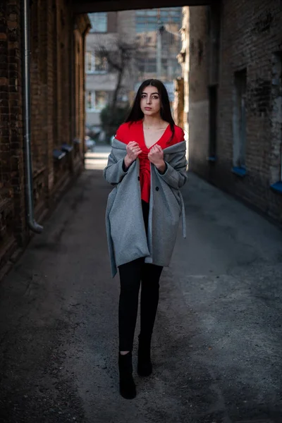 Chica en una blusa roja y un cárdigan gris en el fondo de la vieja pared de ladrillo —  Fotos de Stock