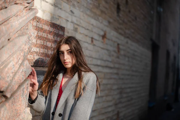 Chica en una blusa roja y un cárdigan gris en el fondo de la vieja pared de ladrillo —  Fotos de Stock