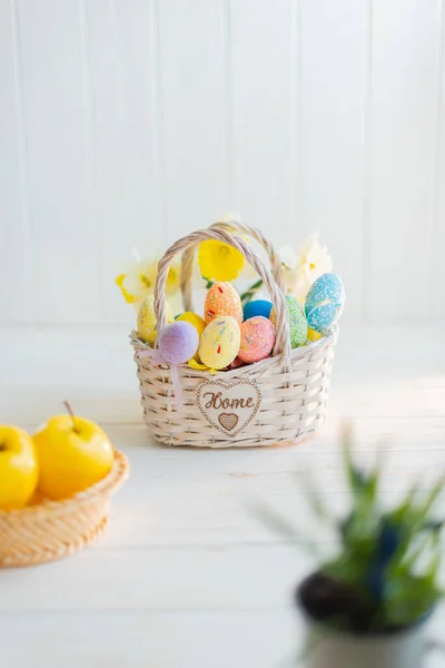 Multi-colored Easter eggs in a basket on a white wooden background