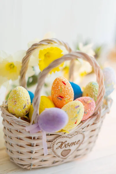 Œufs de Pâques multicolores dans un panier sur un fond en bois blanc — Photo