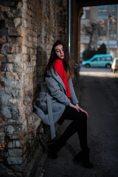 Girl in a red blouse and a gray cardigan on the background of the old brick wall — Stock Photo, Image