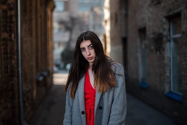 Chica en una blusa roja y un cárdigan gris en el fondo de la vieja pared de ladrillo — Foto de Stock