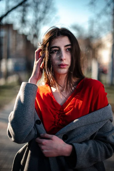 Girl in a red blouse and a gray cardigan on a blurry city background in early spring — Stock Photo, Image