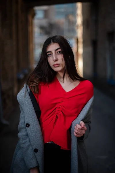 Menina em uma blusa vermelha e um casaco cinza no fundo da parede de tijolo velho — Fotografia de Stock