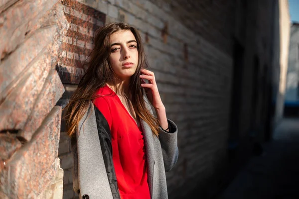 Девушка в красной блузке и сером кардигане на фоне старой кирпичной стены — стоковое фото