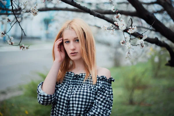 Hermosa joven rubia sobre un fondo de árboles florecientes —  Fotos de Stock