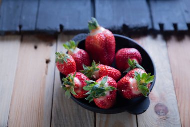 Ahşap bir arka planda siyah bir tabakta çilekler.