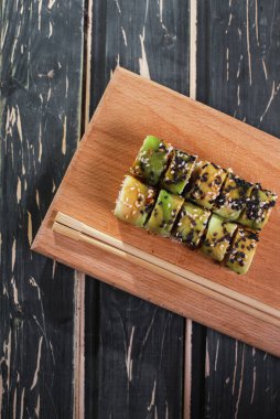 Koyu ahşap arka planda tahta üzerinde somon balıklı suşi.