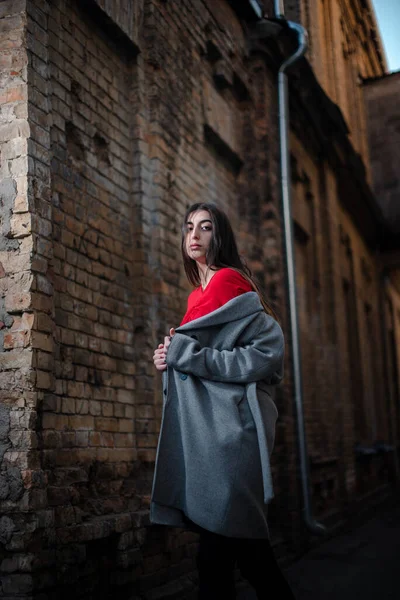 Girl in a red blouse and a gray cardigan on the background of the old brick wall — Stock Photo, Image